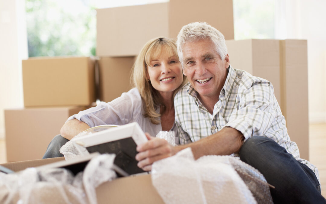 Older couple unpacking pictures in new house, surrounded by boxes