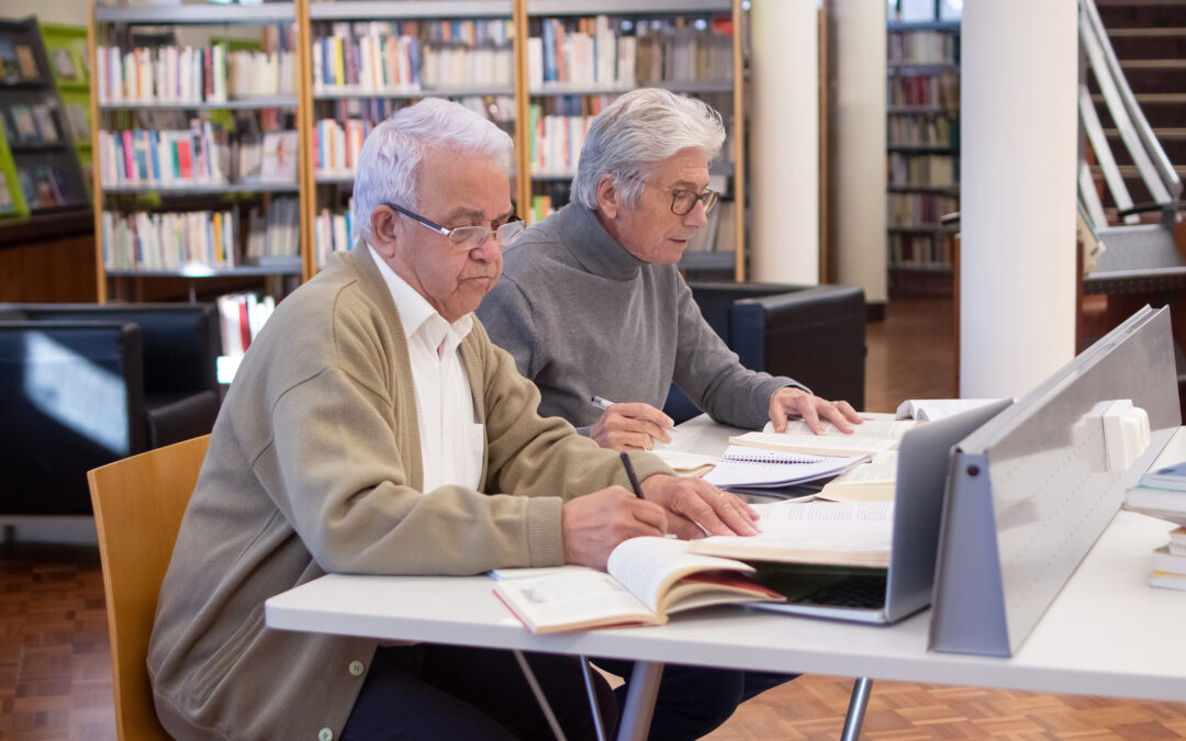 two older people are studying with their computers in the library