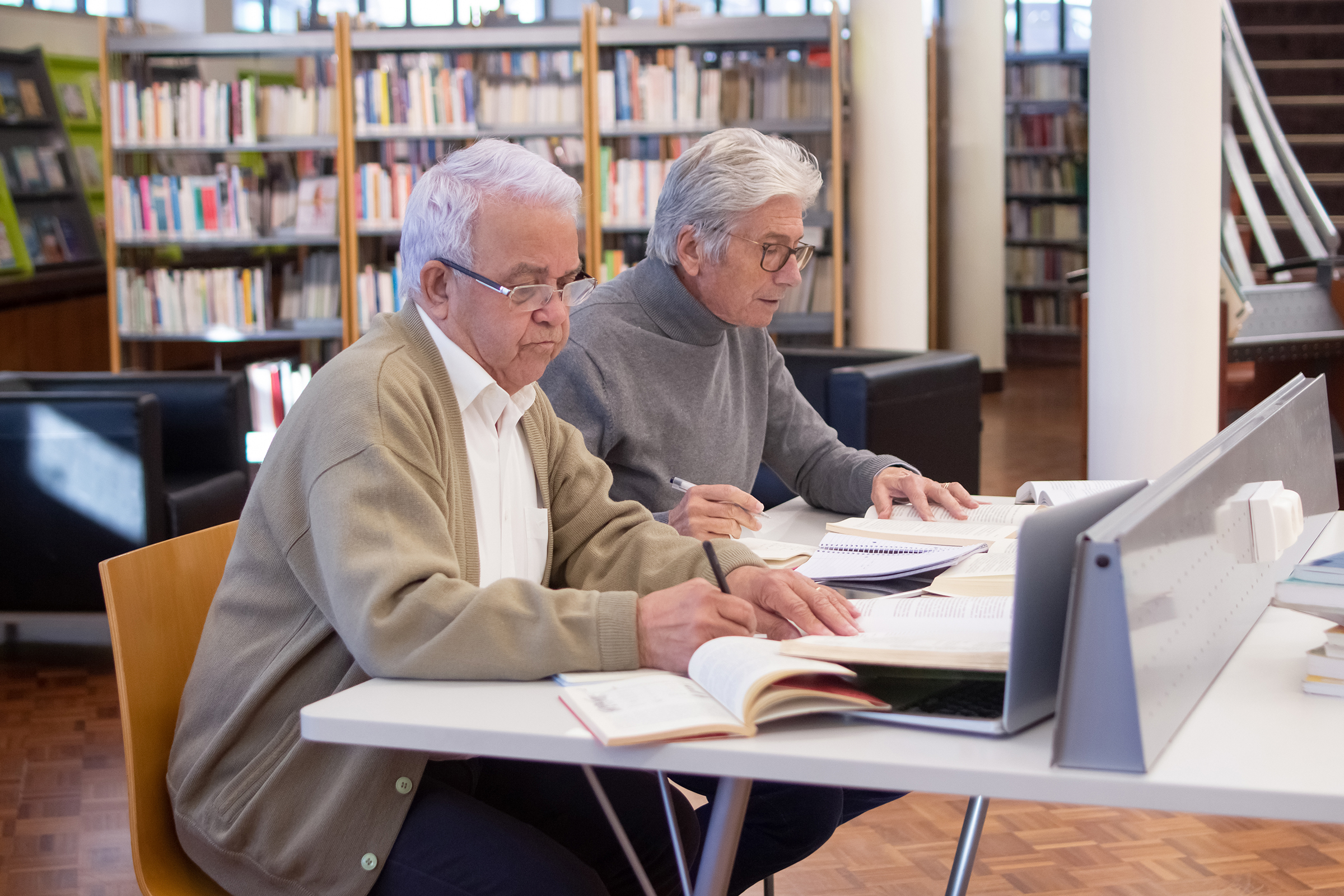 two older people are studying with their computers in the library