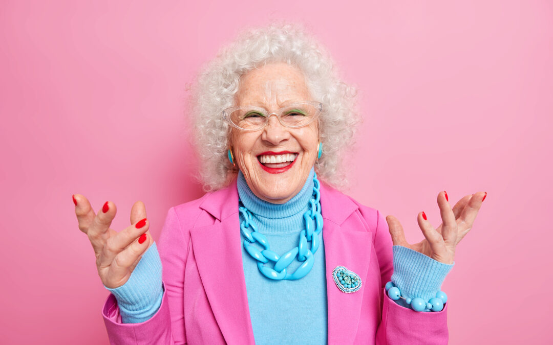 senior woman with a big smile wears a pink blazer and a blue shirt