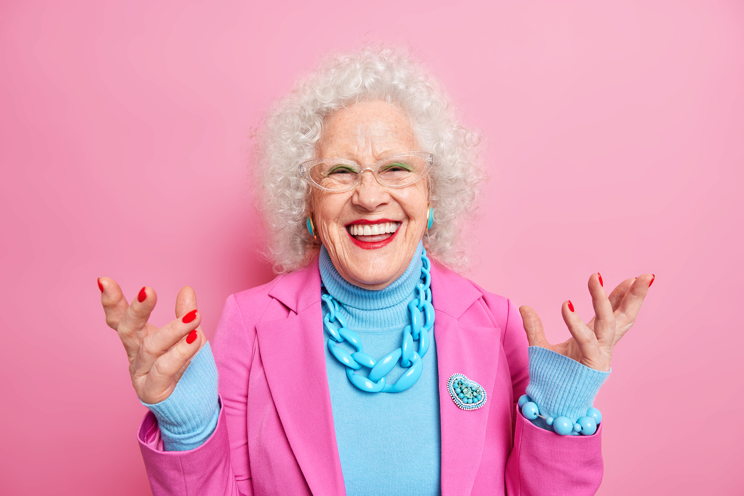 senior woman with a big smile wears a pink blazer and a blue shirt